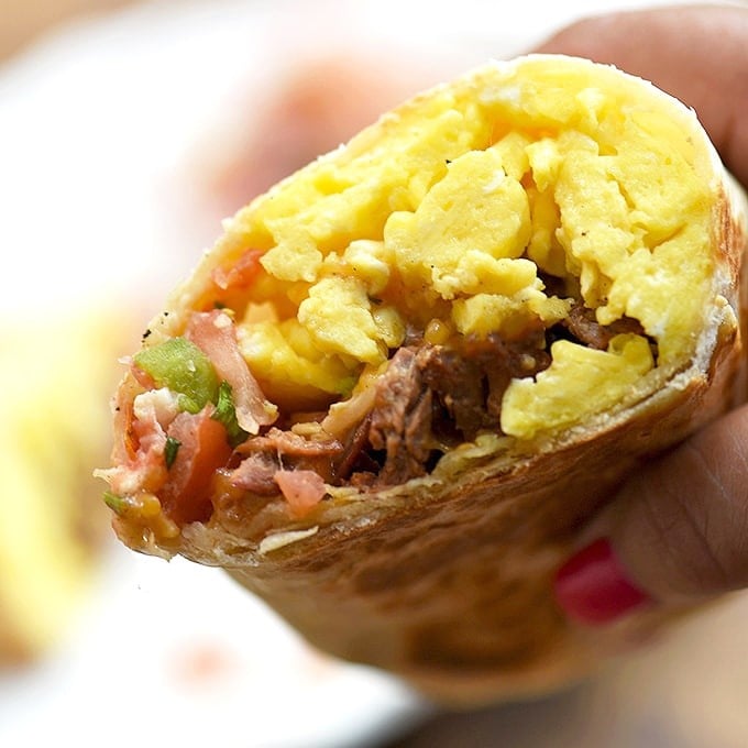 hand holding a breakfast burrito half filled with steak, eggs, and tomato salsa