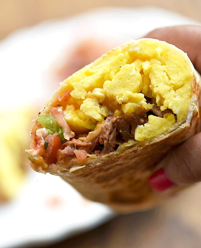 hand holding a breakfast burrito half filled with steak, eggs, and tomato salsa