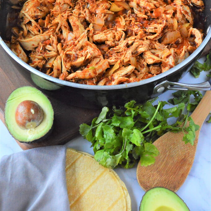 Mexican Chicken Tinga in a pan with sliced avocados, corn tortilla,m and cilantro on the side