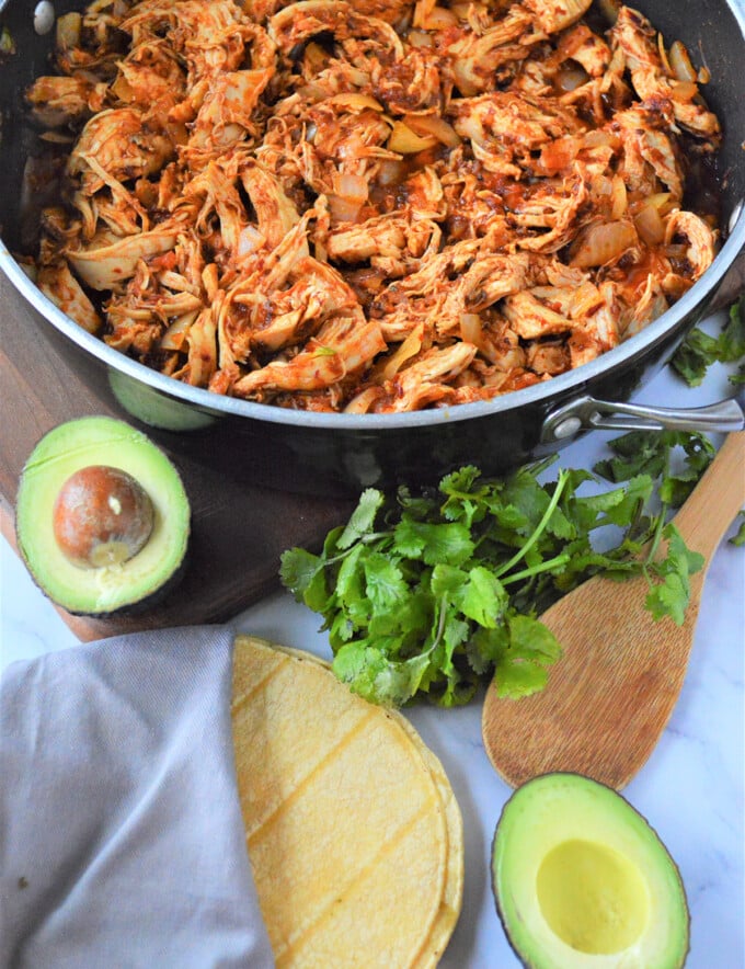 Mexican Chicken Tinga in a pan with sliced avocados, corn tortilla,m and cilantro on the side