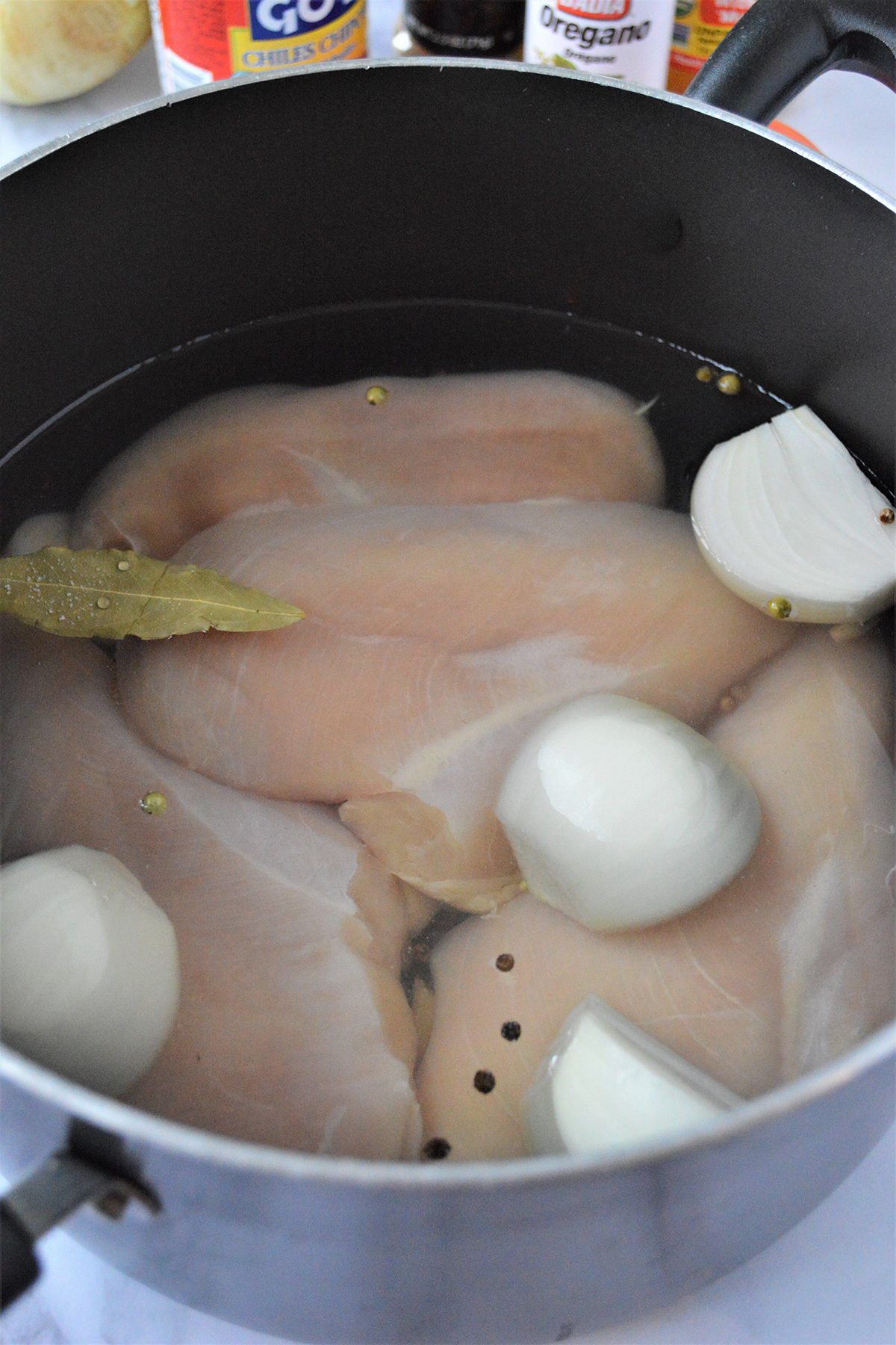 poaching chicken breast in a sauce pot with quartered onions and bay leaf