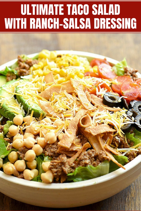 Taco Salad with lettuce, ground beef, avocados, cherry tomatoes, garbanzo beans, olives, tortilla strips and cheese in a white serving bowl