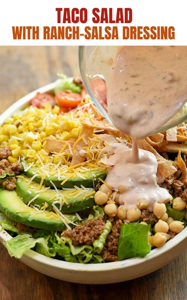 Taco Salad with lettuce, ground beef, avocados, cherry tomatoes, garbanzo beans, olives, tortilla strips and cheese in a white serving bowl