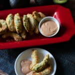 baked avocado fries in a white plate with dipping sauce with red platter with avocado fries on the side