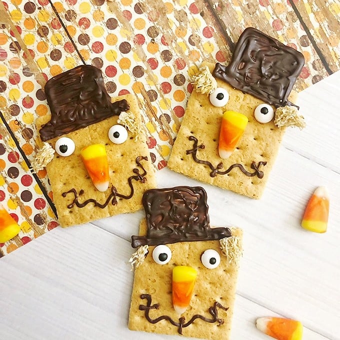 graham crackers decorated as scarecrows with candy corn, melted chocolate and mini wheaties