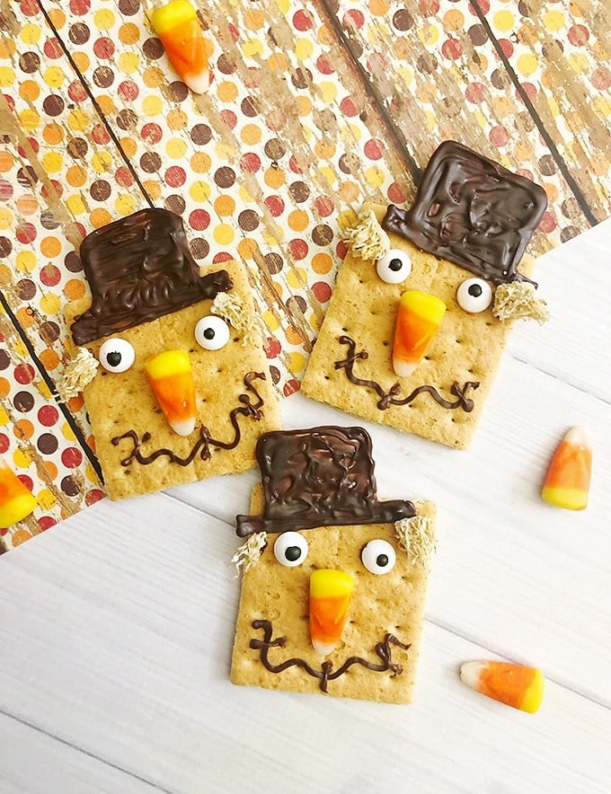 graham crackers decorated as scarecrows with candy corn, melted chocolate and mini wheaties