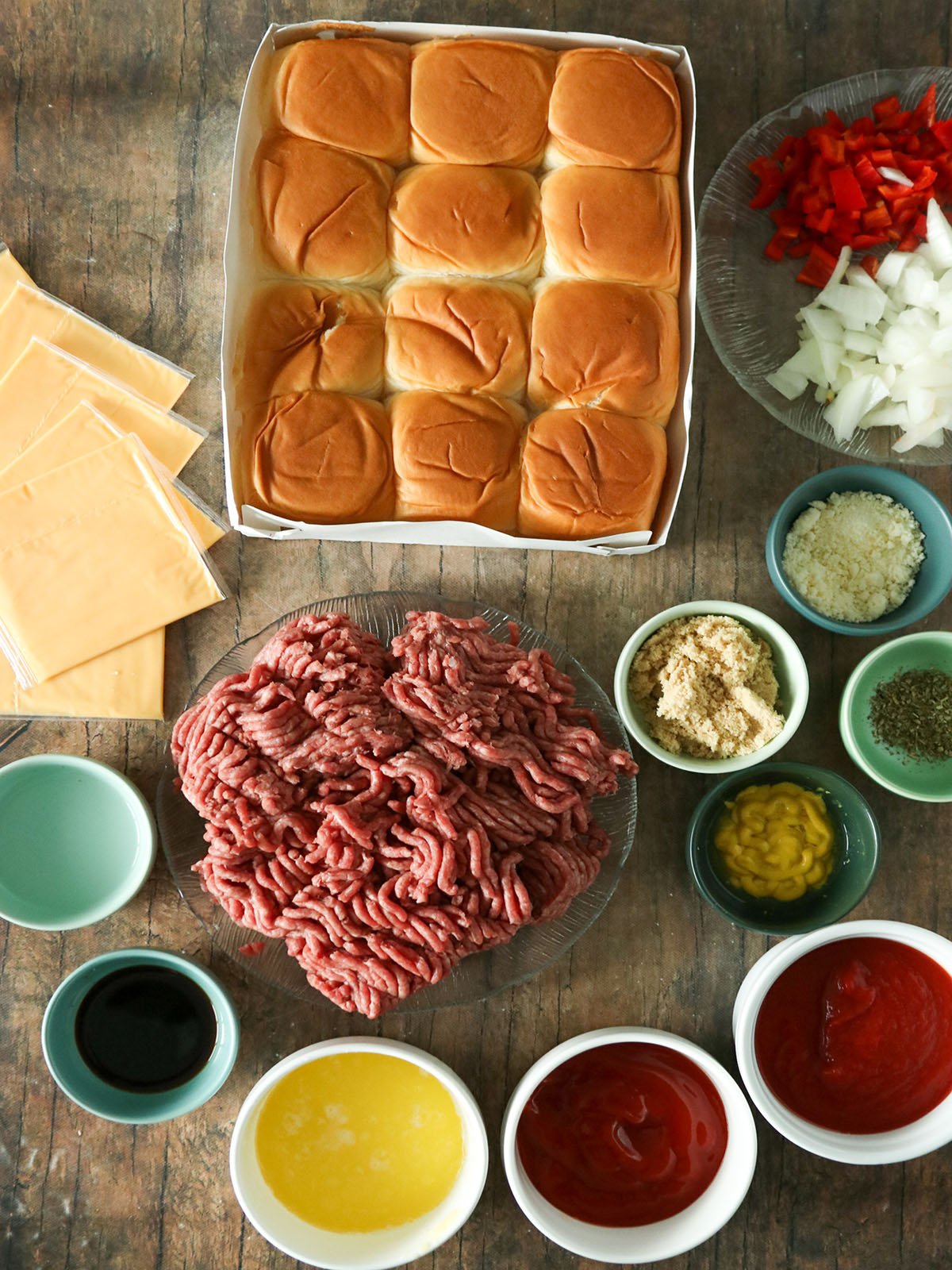 round beef, Hawaiian rolls, cheese, onions, ketchup, mustard, vinegar, salt, pepper, melted butter, brown sugar, tomato sauce, parmesan cheese, Italian seasonings in bowls