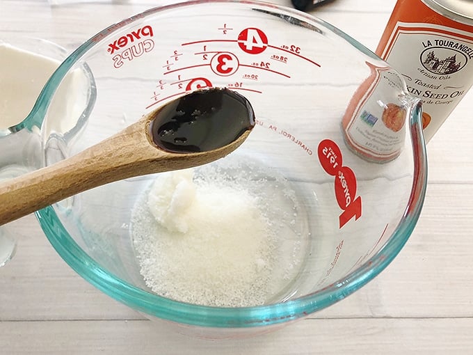 adding pumpkin seed oil into a glass measuring cup with beeswax pellets, cocoa butter, and coconut oil