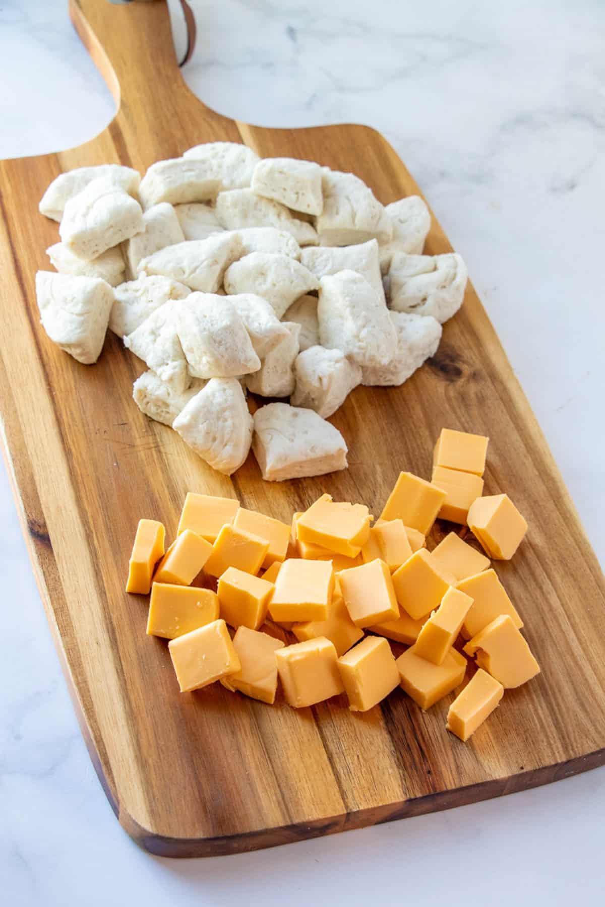 refrigerated biscuits cut into fourths and Velveeta cheese cubes on a wooden cutting board.