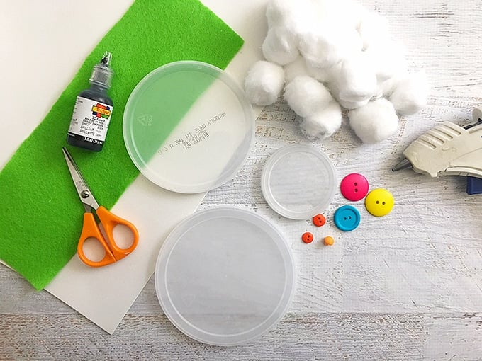 plastic lids, cotton balls, buttons, scissors, and green felt for cotton ball snowman craft