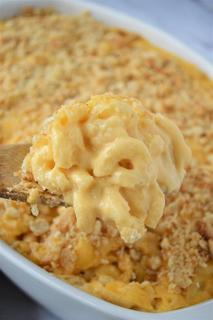 serving mac and cheese with a wooden spoon from a white casserole