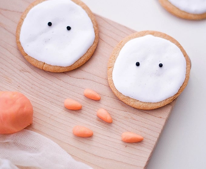 sugar cookies frosted with white royal icing and decorated with black decorating gel and orange fondant to make snowman cookies