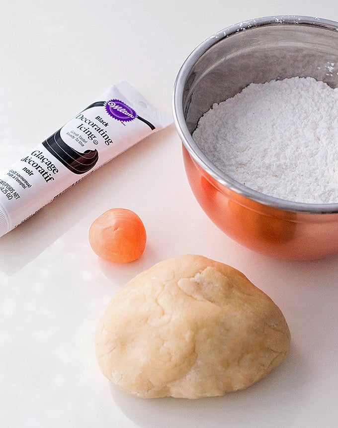 sugar cookie cough, bowl of royal icing powder, orange fondant and tube of decorating gel