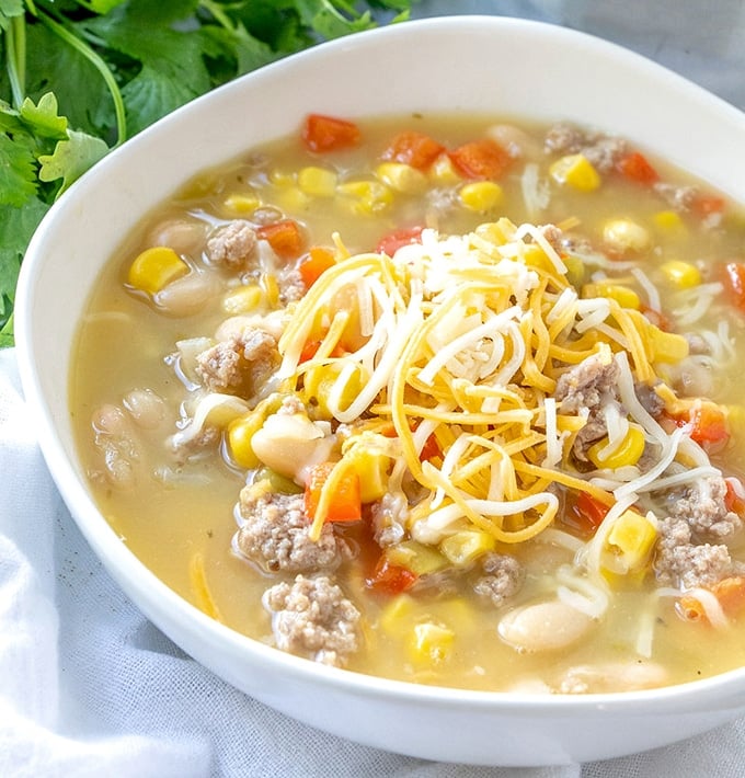 turkey and white bean chili topped with shredded cheese in a white bowl