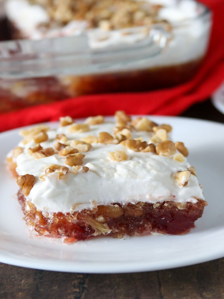 slice of cranberry jello salad with whipped topping on a white plate