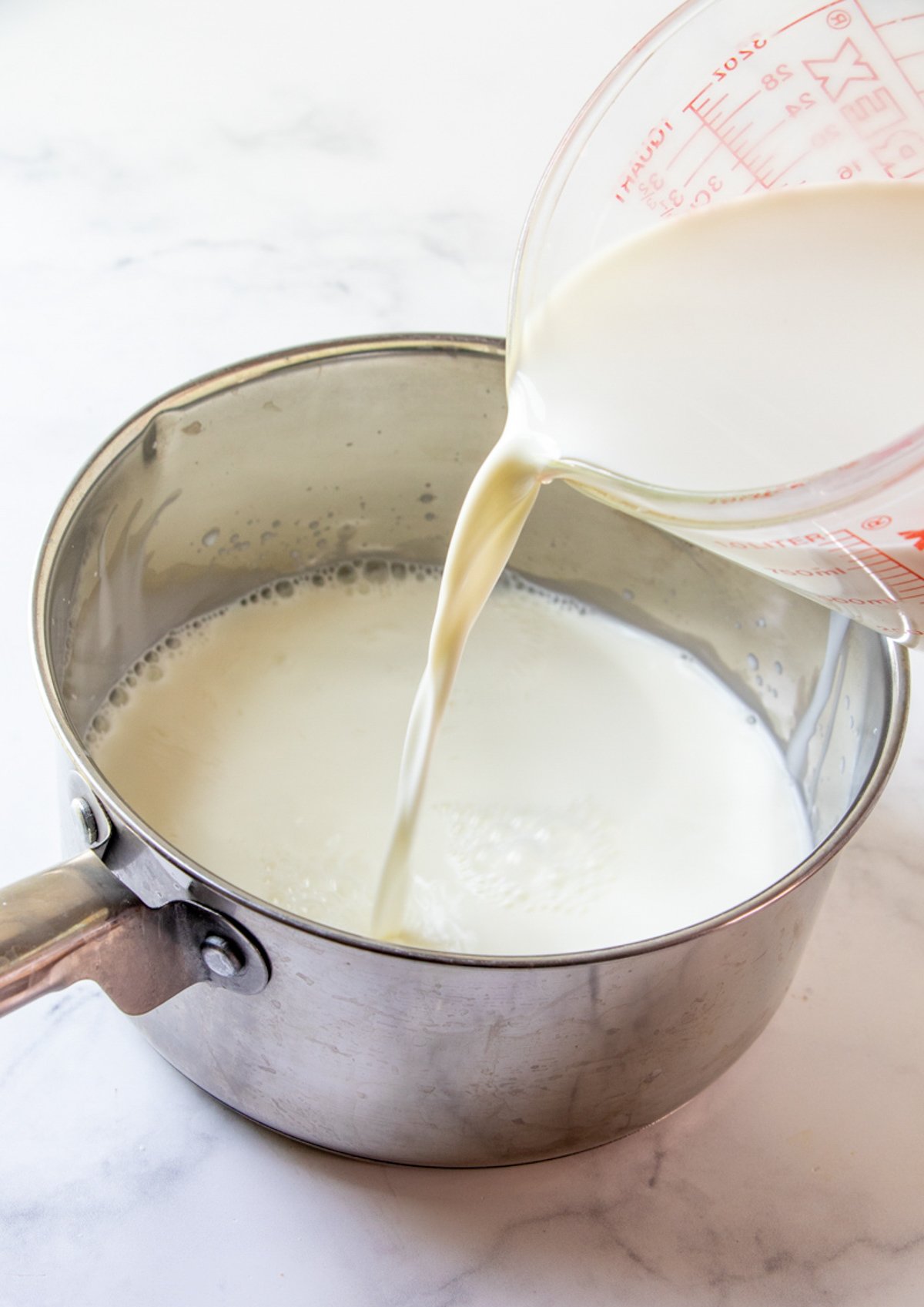 pouring heavy cream to a saucepan of milk