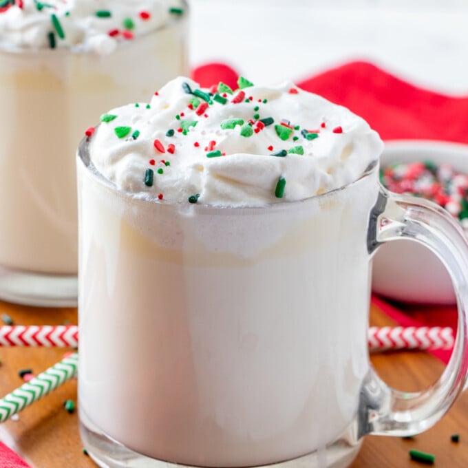 White Hot Chocolate in a clear glass cup, can of whipped topping, and candy sprinkles
