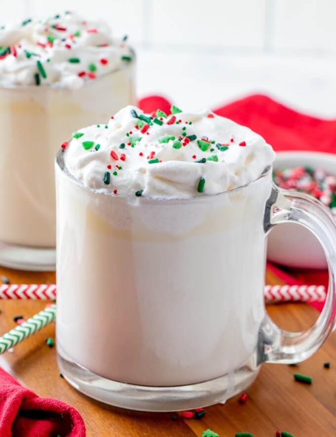 White Hot Chocolate in a clear glass cup, can of whipped topping, and candy sprinkles