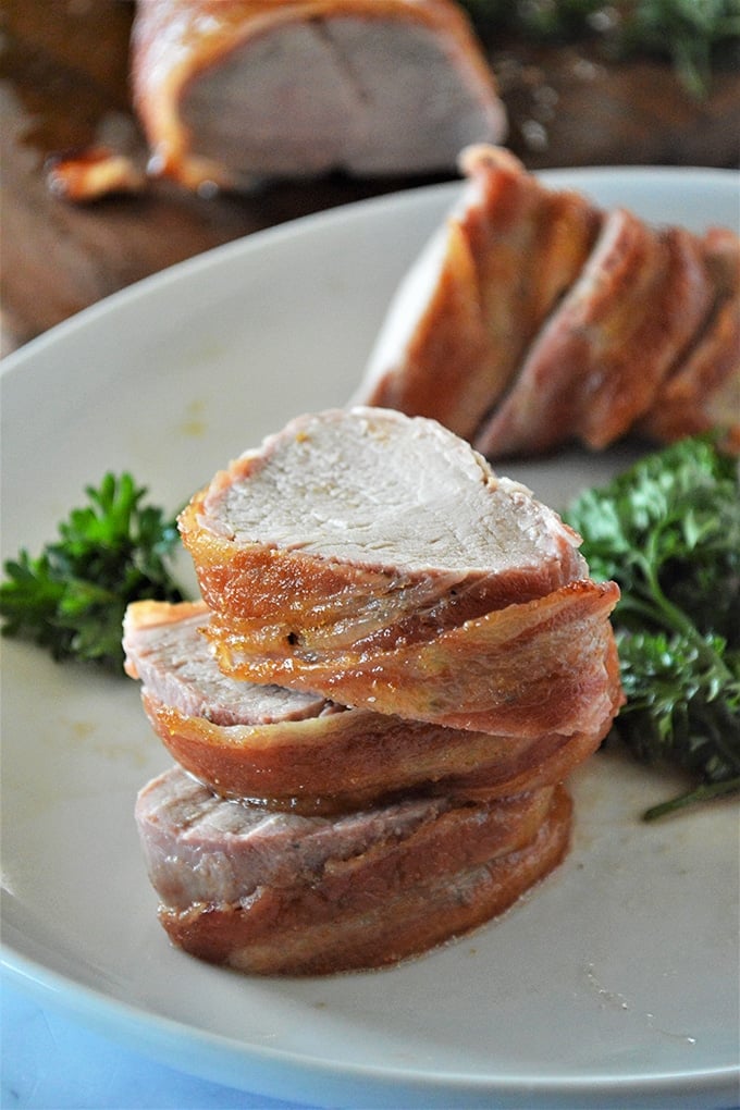 sliced brown sugar pork loin wrapped in bacon on a white plate