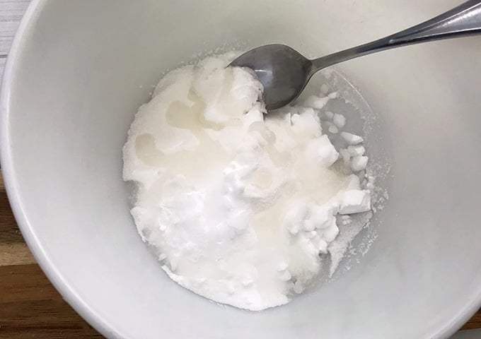 coconut oil added to baking soda and citric acid mixture in a white bowl to make DIY bath bombs