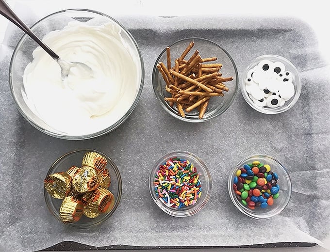 melted white candy melts, candy eyes, mini peanut butter cups, pretzel sticks, mini M&M's on a parchment-lined baking sheet to make snowman candy bark