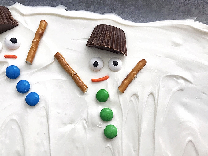 place mini peanut butter cup, candy yes, and orange-colored spinrkles, mini M&M's, pretzel sticks on melted white chocolate to resemble melted snowman 
