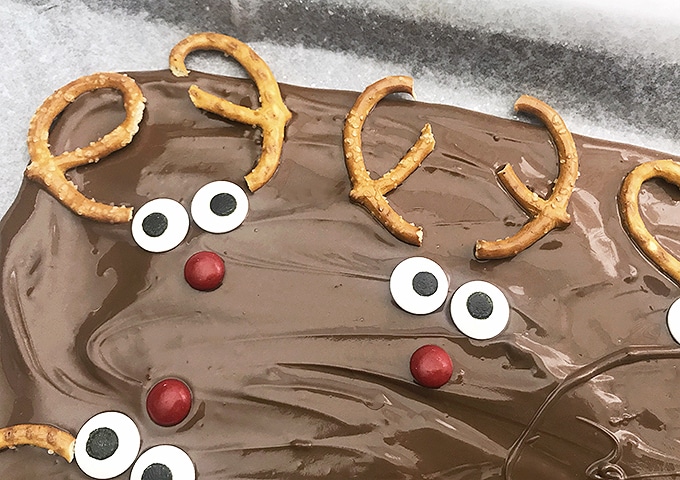 candy eyes, pretzel halves and red M&Ms on thin layer of melted chocolate resembling reindeers