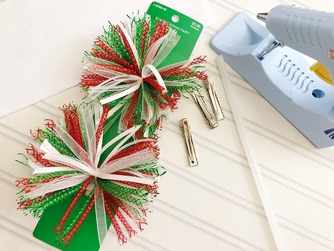 party gift bows, alligator clips, glue gun on a white board for making Christmas hair bows