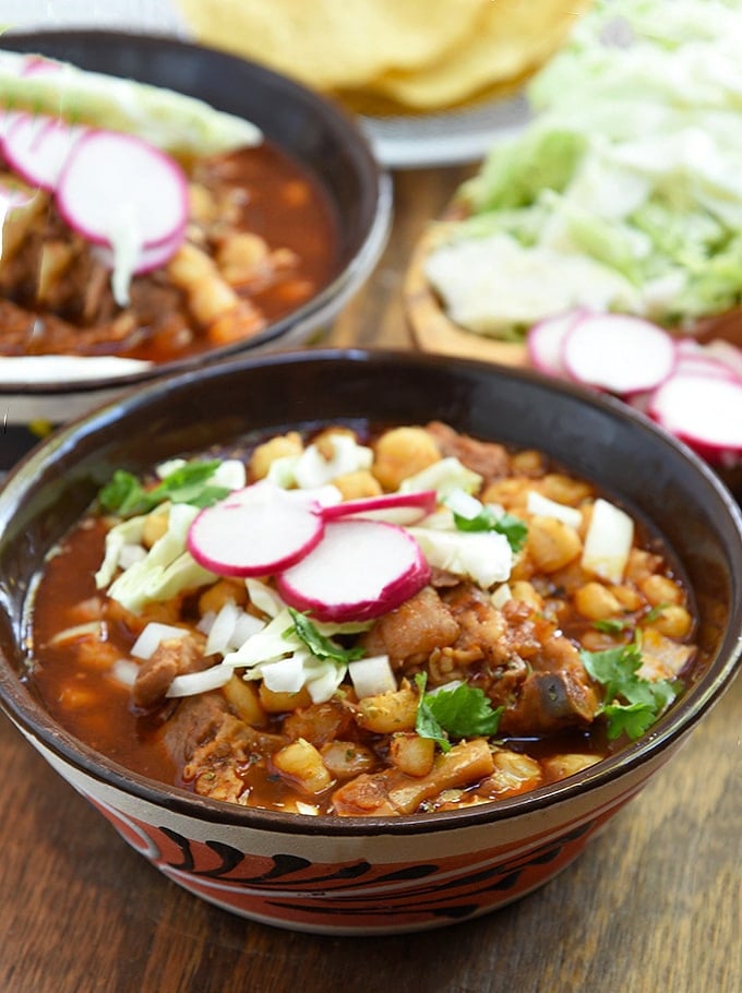 Serve up a delicious bowl of pork pozole rojo topped with radish, cabbage, and onions.