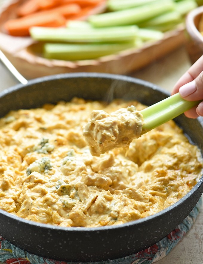 scooping buffalo chicken dip from skillet with a celery stick