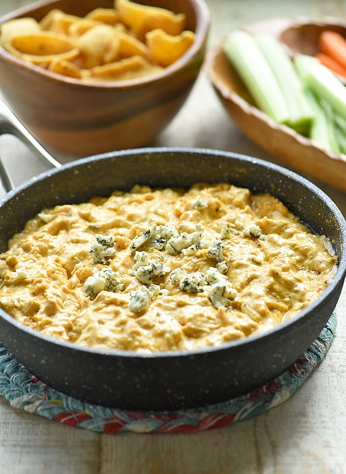 Spicy Buffalo Chicken Dip in a skillet with corn chips and celery and carrot sticks on the side