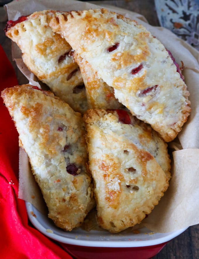 Homemade Cherry Hand Pies in a cloth-lined basket with fresh cherries on the side