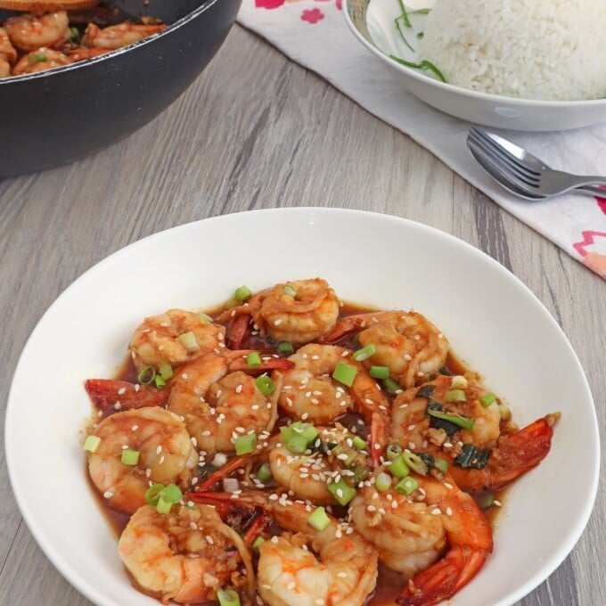 Shrimp in Soy Sauce in a white bowl with a black pan and a plate of steamed rice on the side