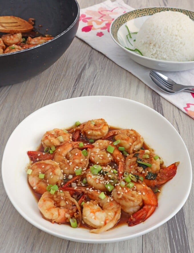 Shrimp in Soy Sauce in a white bowl with a black pan and a plate of steamed rice on the side