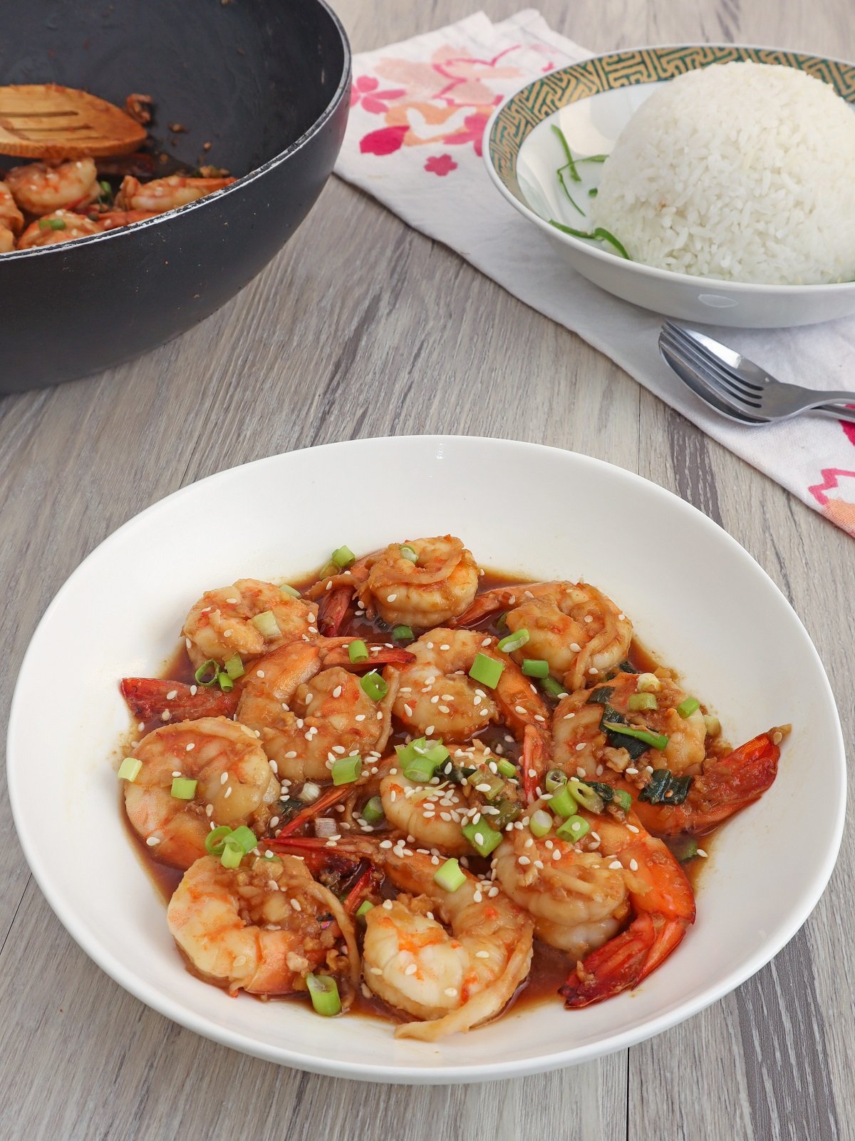 Shrimp in Soy Sauce in a white bowl with a black pan and a plate of steamed rice on the side