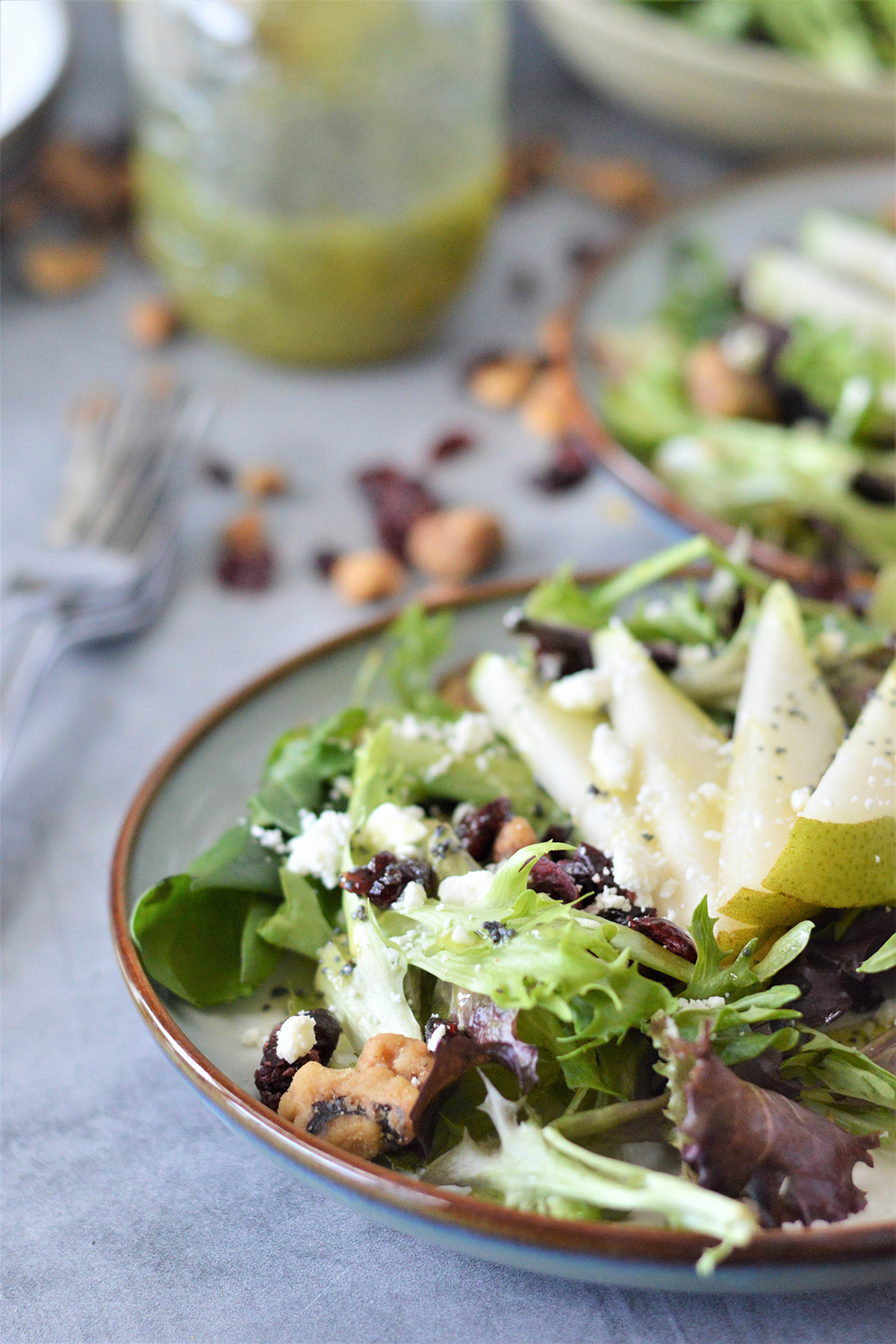 salad with sliced pears, feta cheese, candied walnuts, and cranberries on a serving plate with homemade dressing on the side