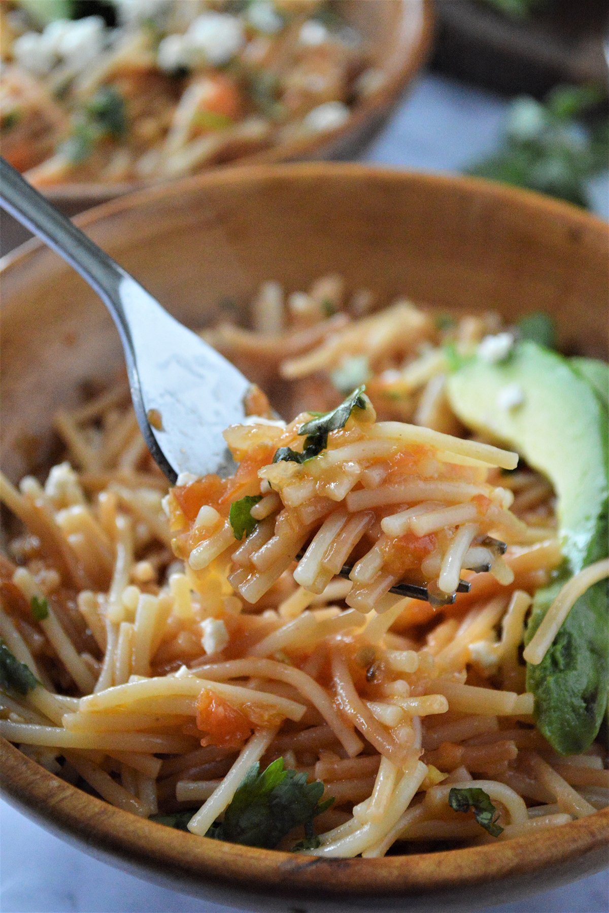 eating Mexican fideo seco with a fork from a wooden bowl