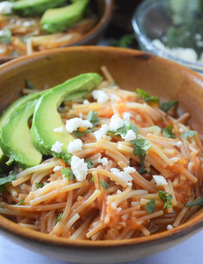 Sopa Seca de Fideo with avocadoes and crumbled cheese in a wooden bowl