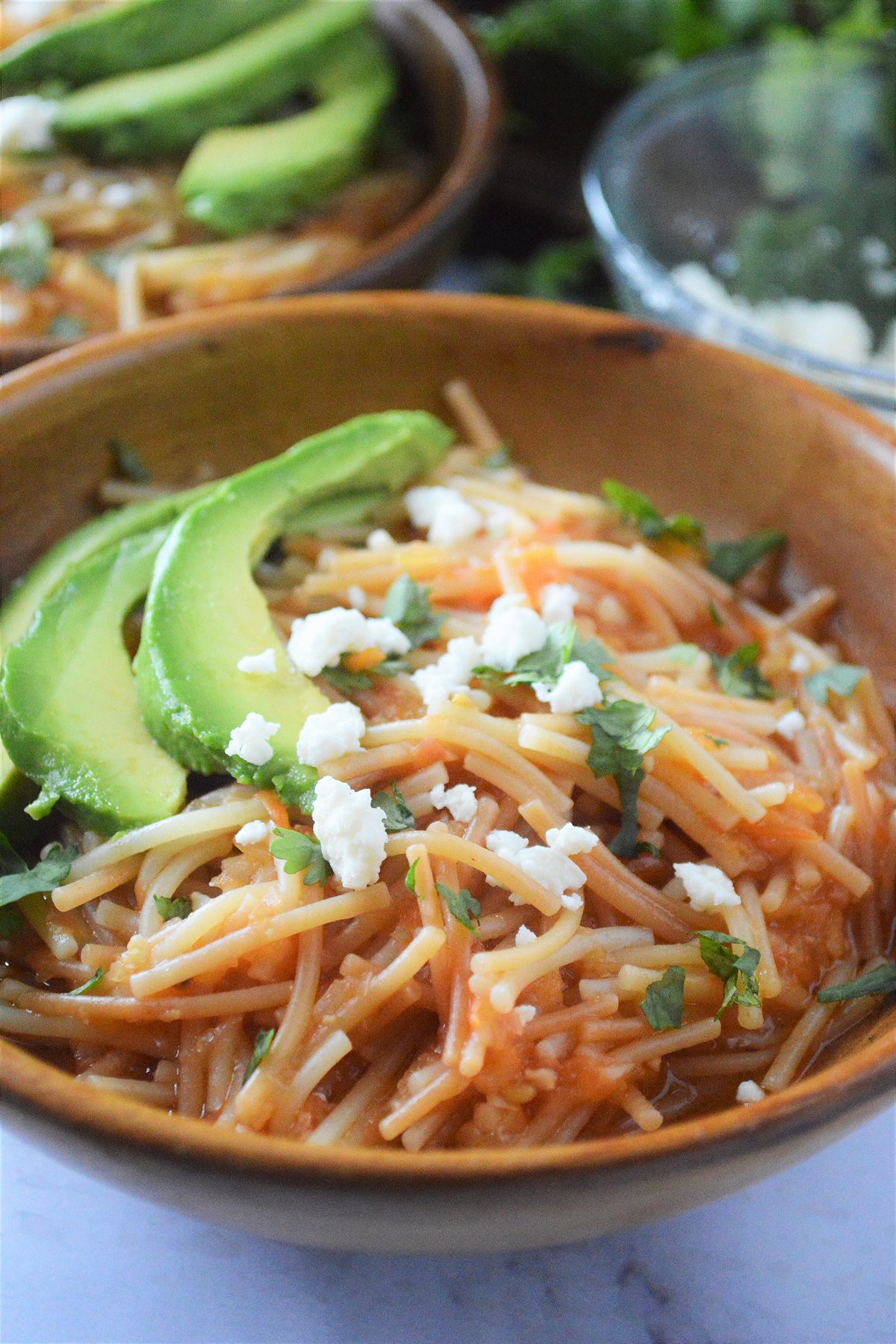 Sopa Seca de Fideo with avocadoes and crumbled cheese in a wooden bowl