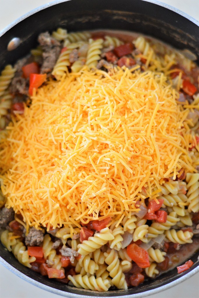 pasta, tomatoes, beef, shredded cheese in a pot