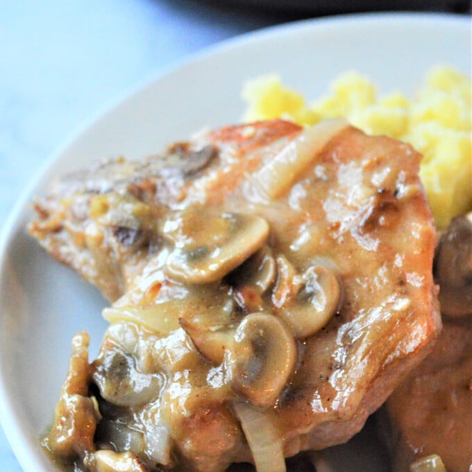 Smothered Pork Chops with Mushroom Gravy with mashed potatoes on a white plate