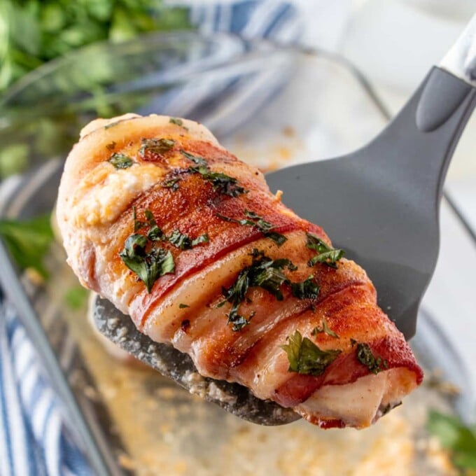 serving bacon-wrapped cheese-stuffed chicken with a spatula.