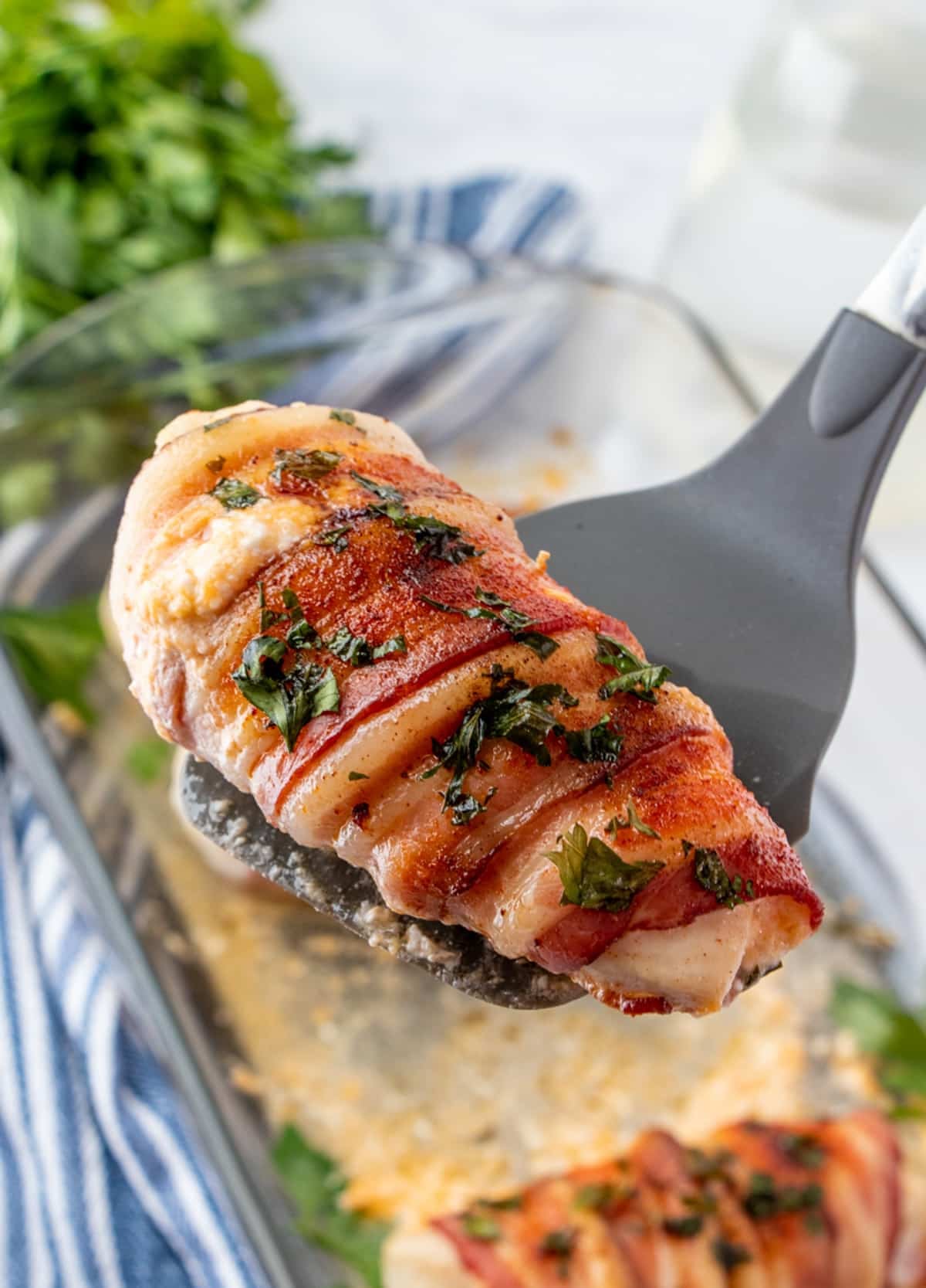 serving bacon-wrapped cheese-stuffed chicken with a spatula.