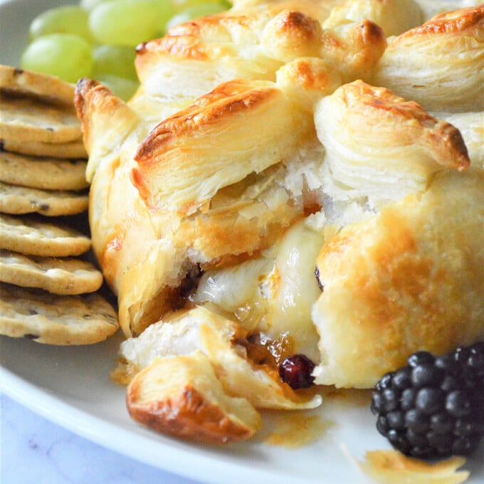cut Brie en Croute with fresh berries and crackers on a white platter