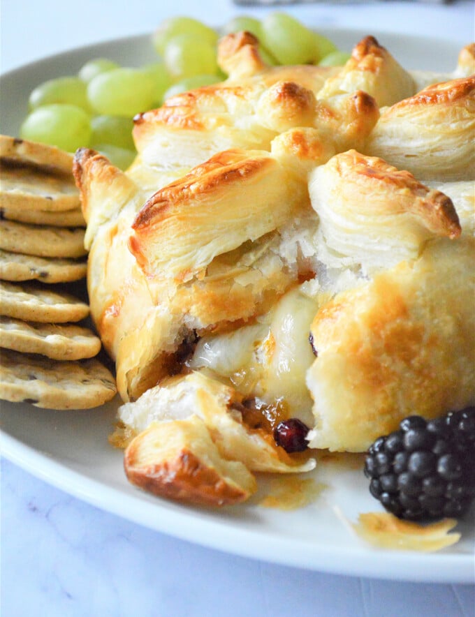 cut Brie en Croute with fresh berries and crackers on a white platter