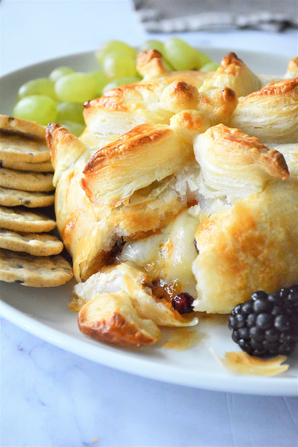 cut Brie en Croute with fresh berries and crackers on a white platter