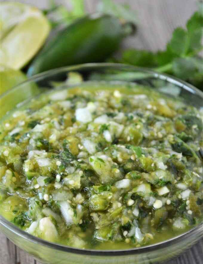 Salsa Verde in a glass bowl with jalapeno and cilantro in the background.